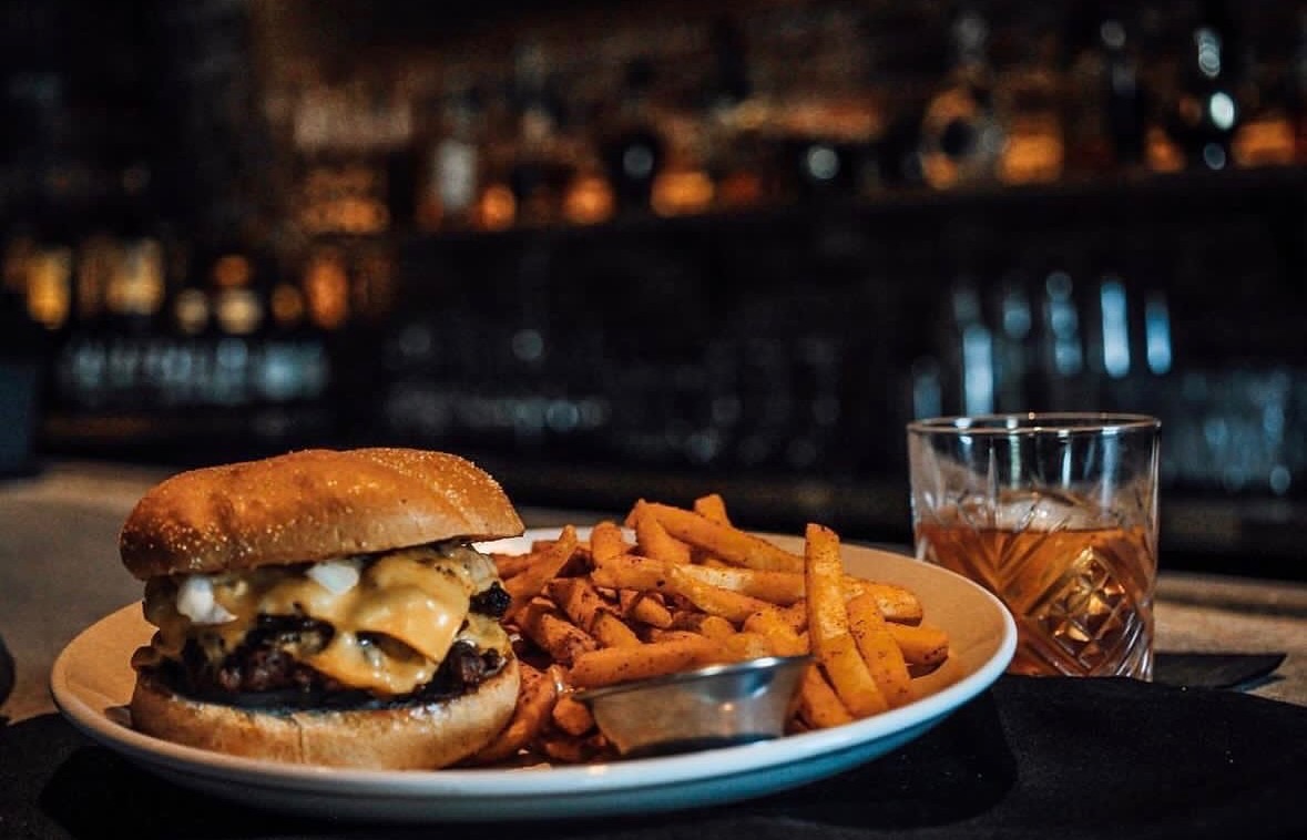 A double smash burger with hand cut fries and a pour of bourbon at the bar at Whiskey & Water