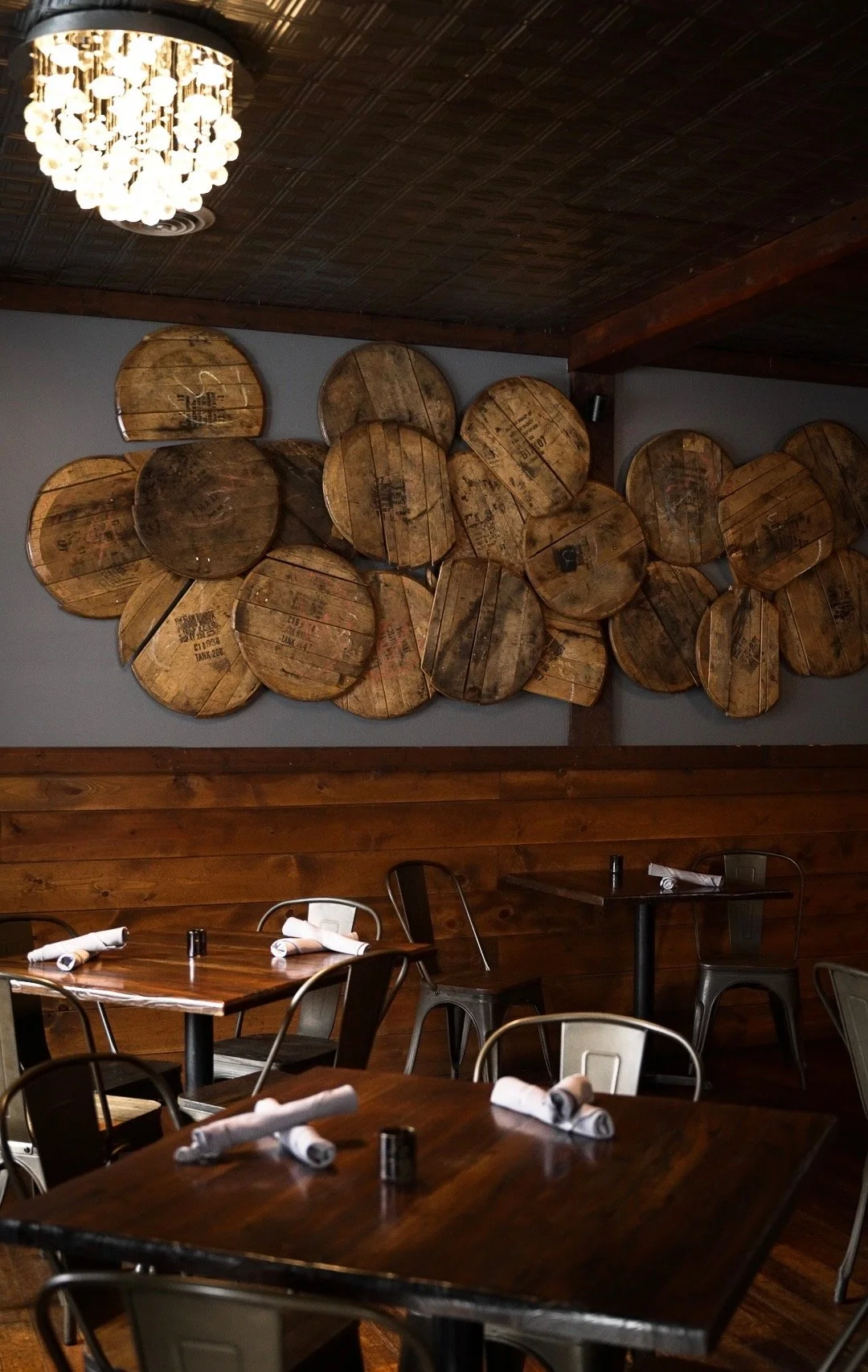 Whiskey & Water dining room in Blue Ridge, GA, with a wall of bourbon barrel heads beneath the original 1937 tin ceiling